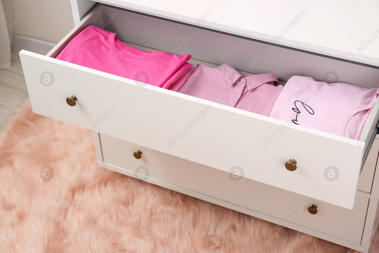 Photo of Many folded pink clothes in white chest of drawers indoors