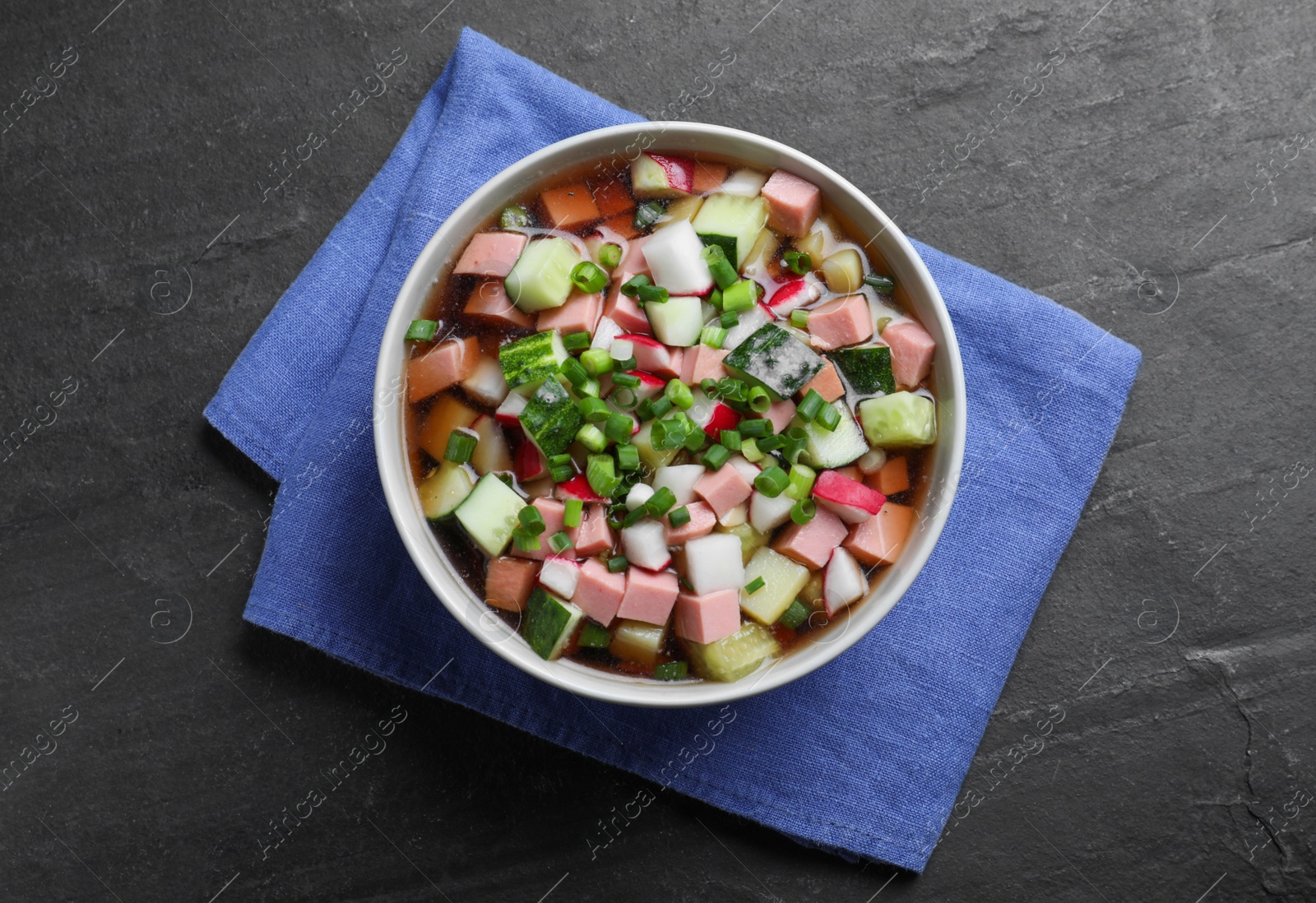 Photo of Delicious cold okroshka with kvass on black table, top view. Traditional Russian summer soup