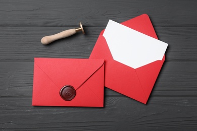 Envelopes with wax seal and stamp on black wooden background, flat lay