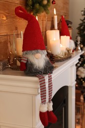 Photo of Cute Christmas gnome and festive decorations on mantelpiece in room