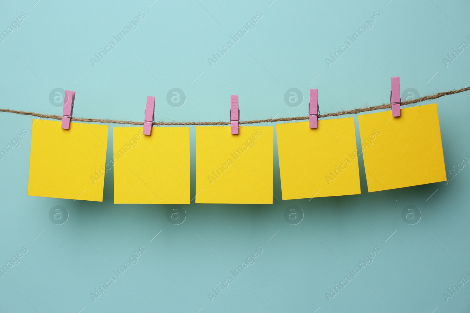 Photo of Wooden clothespins with blank notepapers on twine against light blue background. Space for text