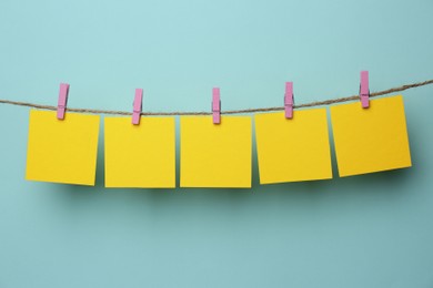 Wooden clothespins with blank notepapers on twine against light blue background. Space for text