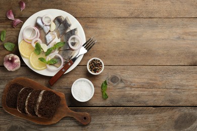 Sliced salted herring fillet served with basil, onion rings and lemon on wooden table, flat lay. Space for text
