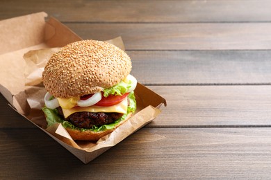 Photo of Delicious burger in cardboard box on wooden table. Space for text