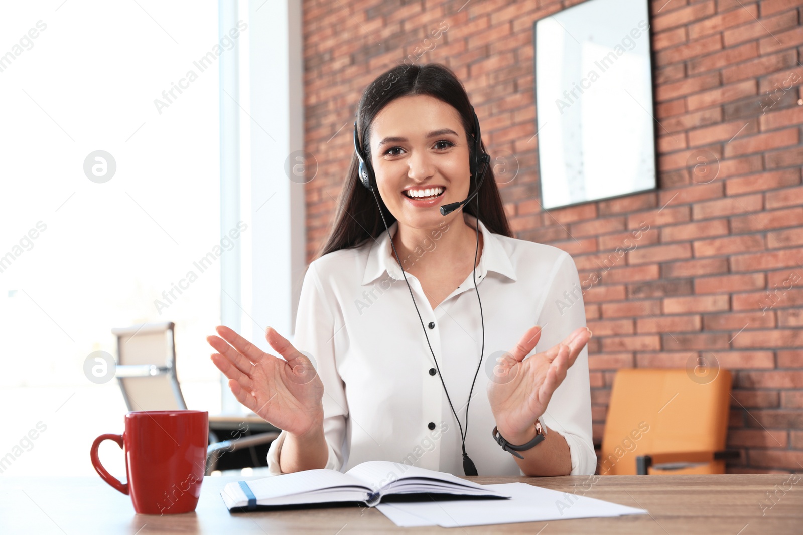 Photo of Young woman with headset looking at camera and using video chat in home office