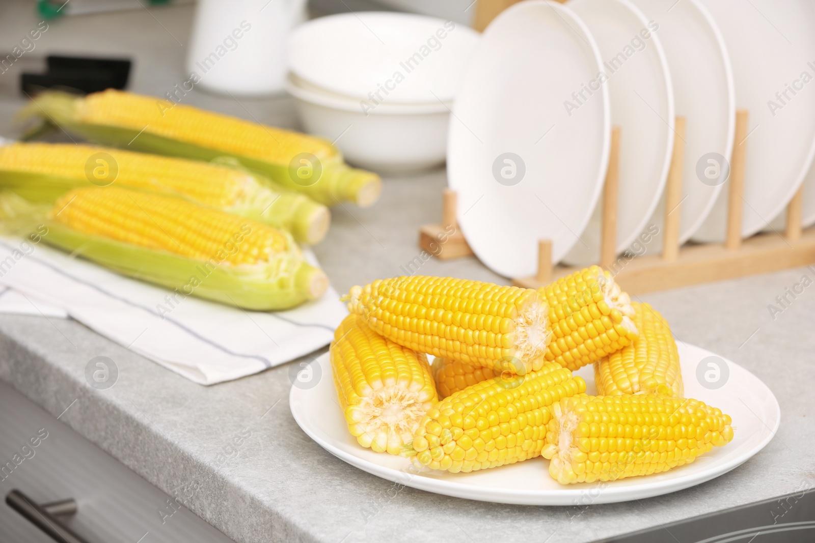 Photo of Plate with ripe corn cobs on kitchen table