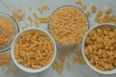 Different types of pasta on white marble table, flat lay