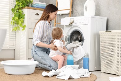 Mother with her daughter washing baby clothes in bathroom