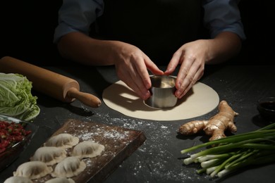 Woman cutting dough for gyoza at grey table, closeup