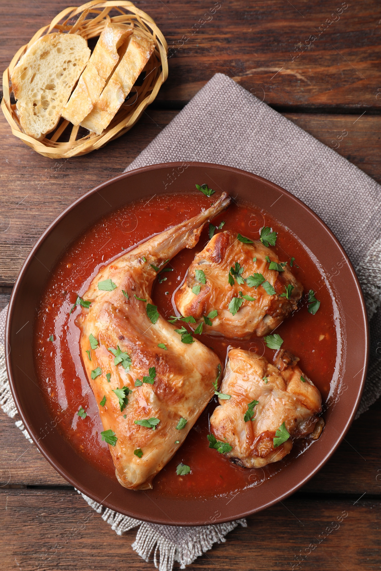 Photo of Tasty cooked rabbit meat with sauce and bread on wooden table, top view