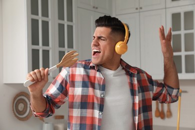 Photo of Man with headphones and fork spatula singing in kitchen
