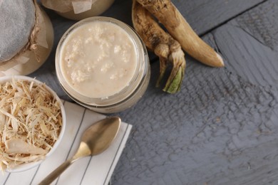 Spicy horseradish sauce in jars, roots and spoon on grey wooden table, flat lay. Space for text