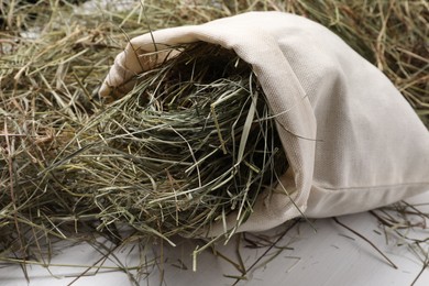 Burlap sack with dried hay on white wooden table, closeup