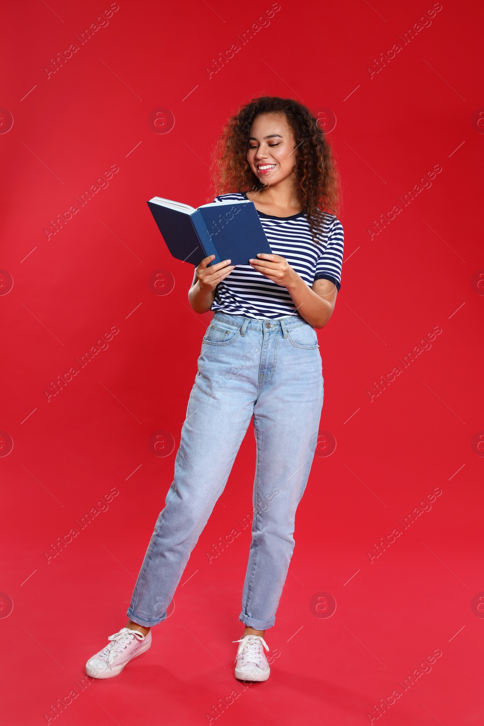 Photo of Beautiful African-American young woman reading book on red background