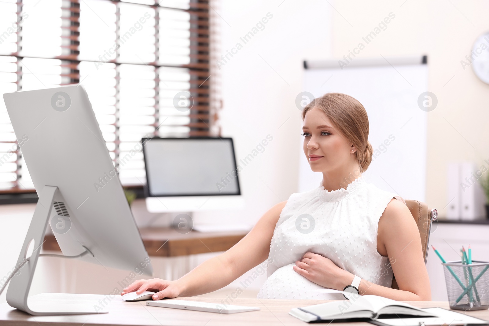 Photo of Young pregnant woman working with computer at table in office