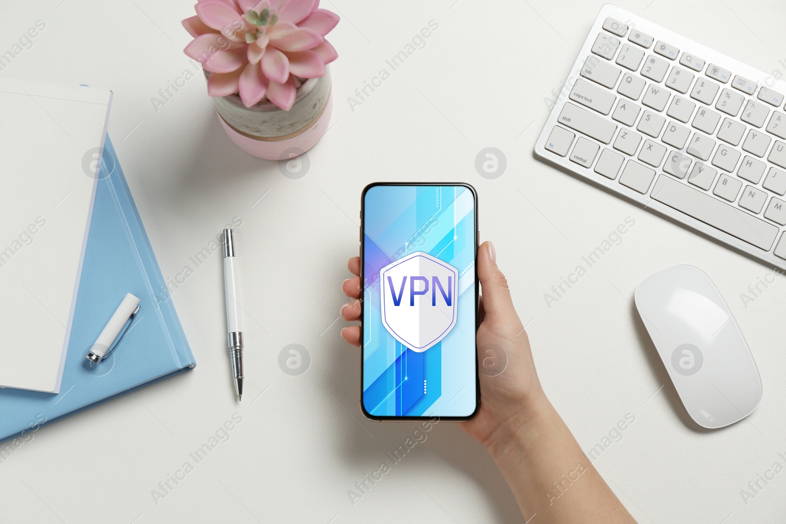 Image of Woman holding smartphone with switched on VPN at white table, top view