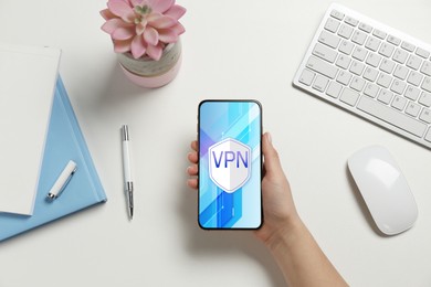 Image of Woman holding smartphone with switched on VPN at white table, top view
