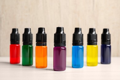 Photo of Glass bottles with different food coloring on white wooden table