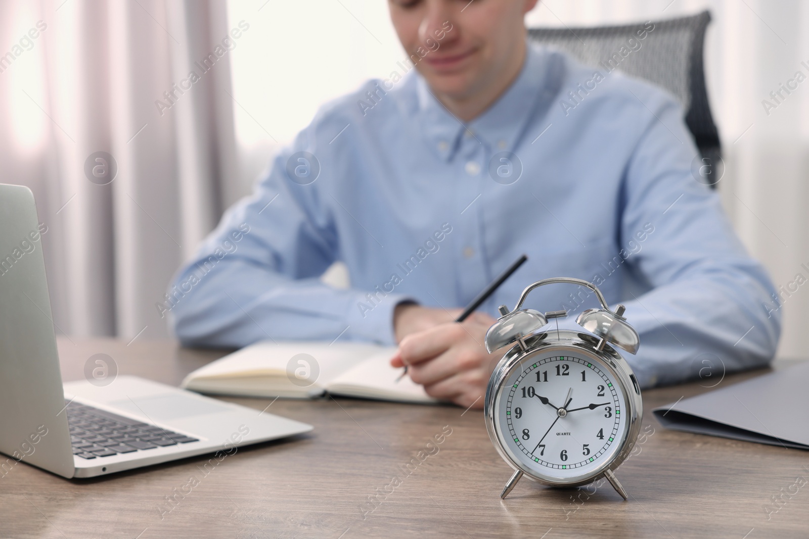 Photo of White alarm clock and man working at table, closeup