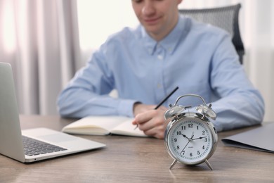 Photo of White alarm clock and man working at table, closeup