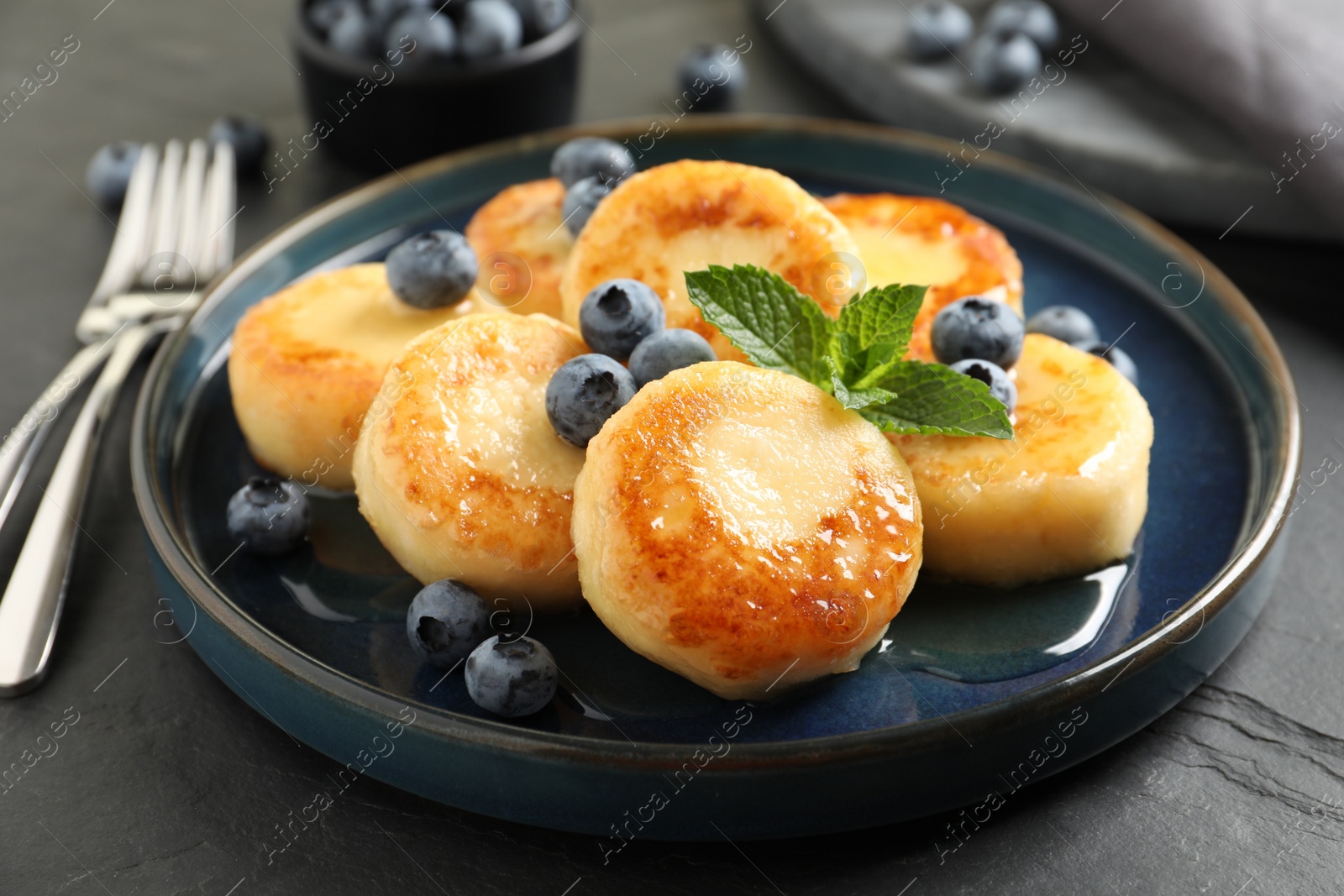 Photo of Delicious cottage cheese pancakes with blueberries on black table, closeup