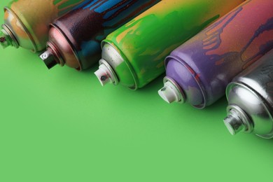 Photo of Used cans of spray paints on green background, closeup with space for text. Graffiti supplies