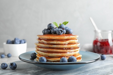 Plate of delicious pancakes with fresh blueberries and syrup on grey table against light background