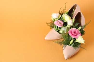 Photo of Stylish women's high heeled shoes with beautiful flowers on pale orange background, space for text