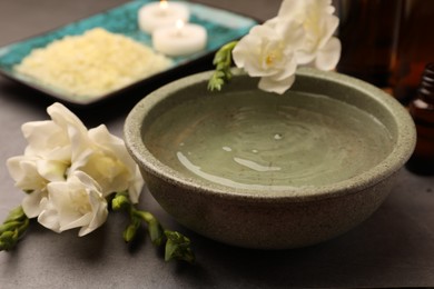 Bowl of essential oil and beautiful flowers on grey table, closeup. Aromatherapy treatment