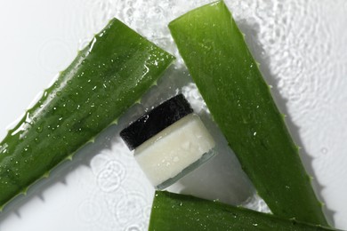 Photo of Jar of cosmetic product and aloe leaves in water on white background, flat lay