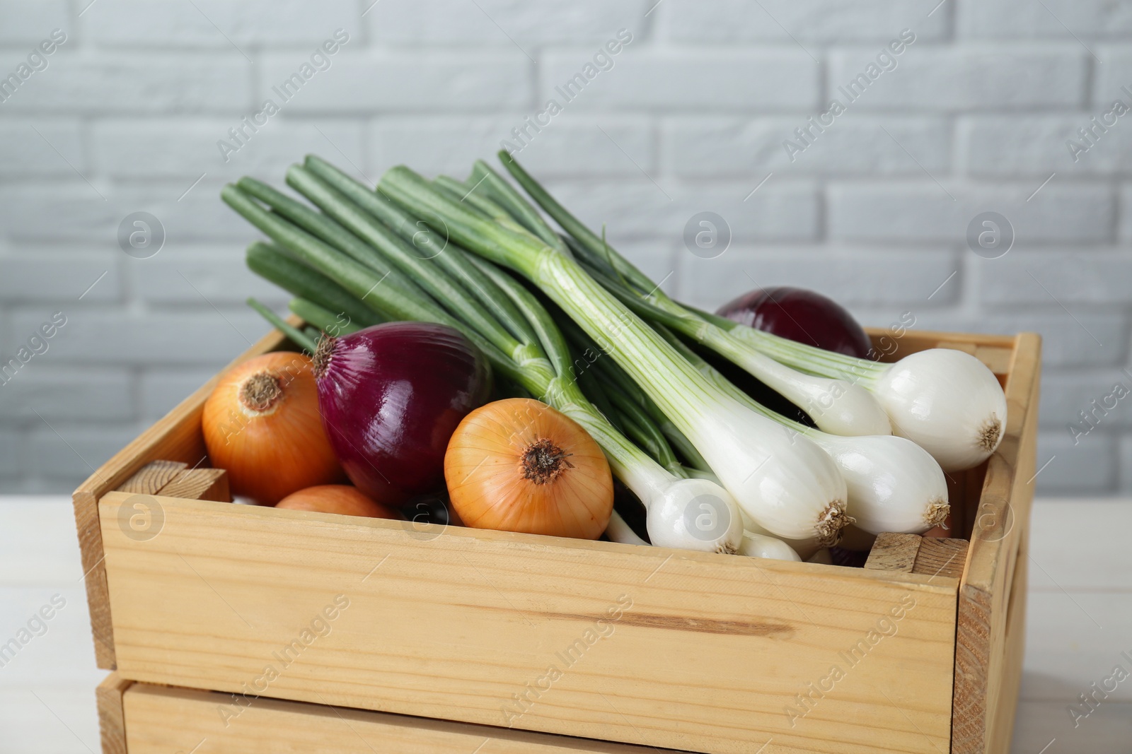 Photo of Crate with different kinds of onions on white table, closeup