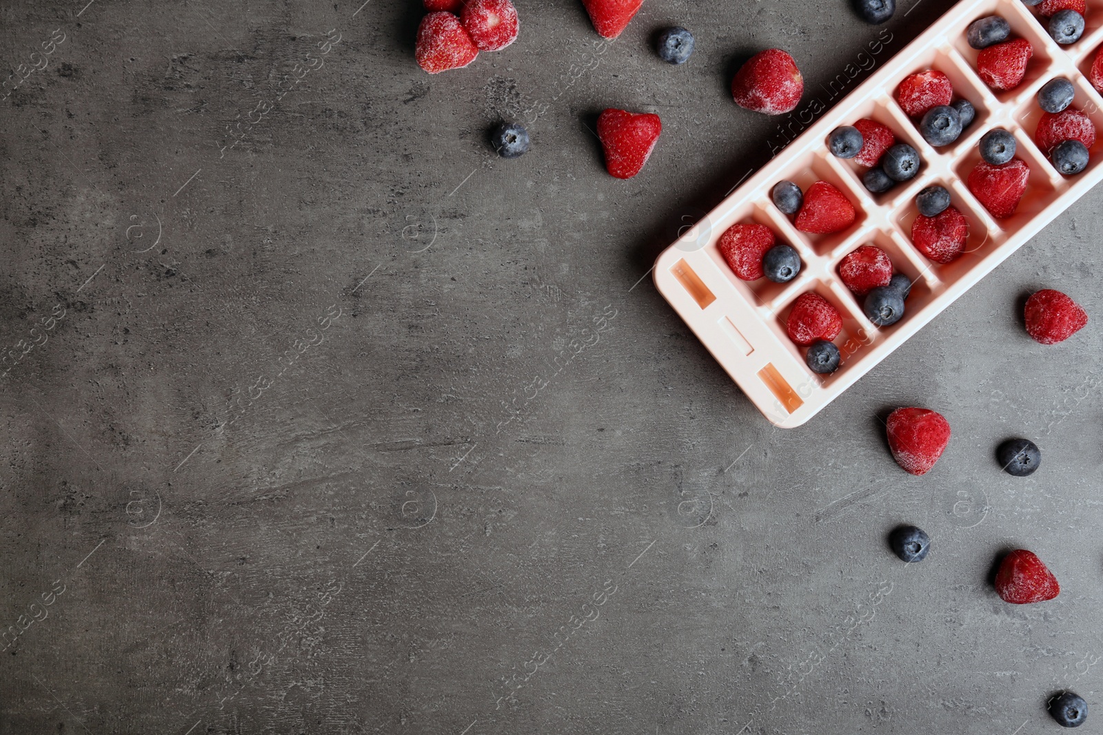 Photo of Flat lay composition with ice cube tray and frozen berries on grey background. Space for text