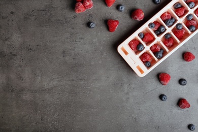 Photo of Flat lay composition with ice cube tray and frozen berries on grey background. Space for text