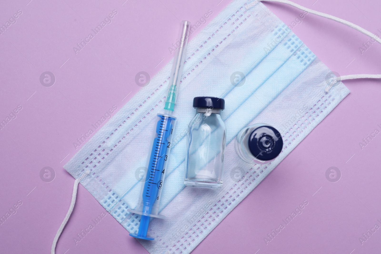 Photo of Disposable syringe, vials with medicine and protective mask on violet background, flat lay