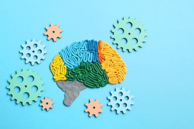 Amnesia problem. Brain with sections made of plasticine and gears on light blue background, flat lay