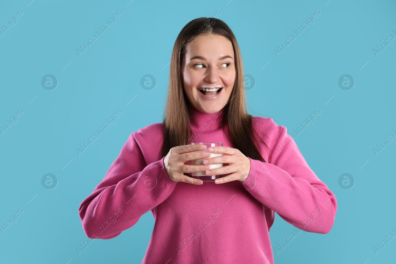 Photo of Happy woman with milk mustache holding glass of drink on light blue background