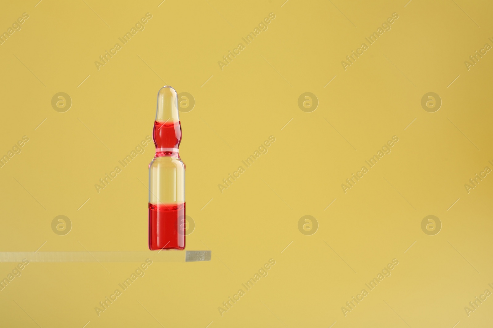 Photo of Glass ampoule with liquid on yellow background. Space for text