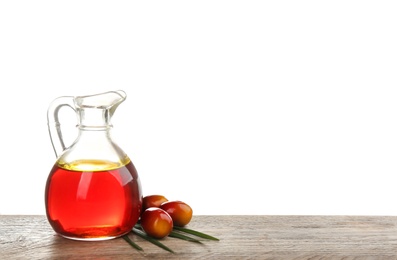 Palm oil in glass jug, tropical leaf and fruits on wooden table against white background