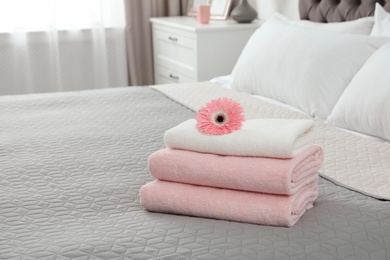 Stack of clean towels with flower on bed indoors. Space for text