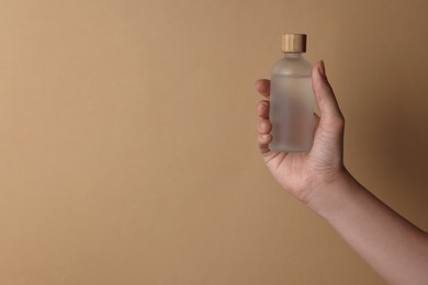 Photo of Woman holding bottle of cosmetic product on beige background, closeup. Space for text