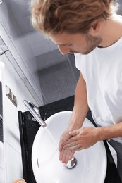 Young man washing hands with soap over sink in bathroom