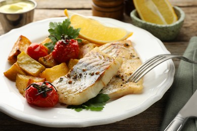 Tasty cod cooked with vegetables served on wooden table, closeup