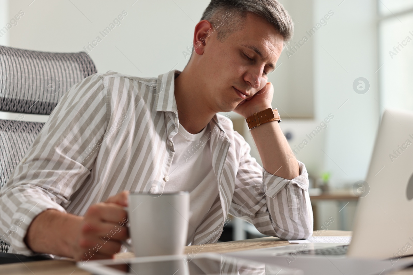 Photo of Man with cup of drink snoozing at table in office