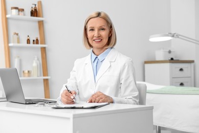 Photo of Portrait of happy dermatologist with pen at white table in clinic