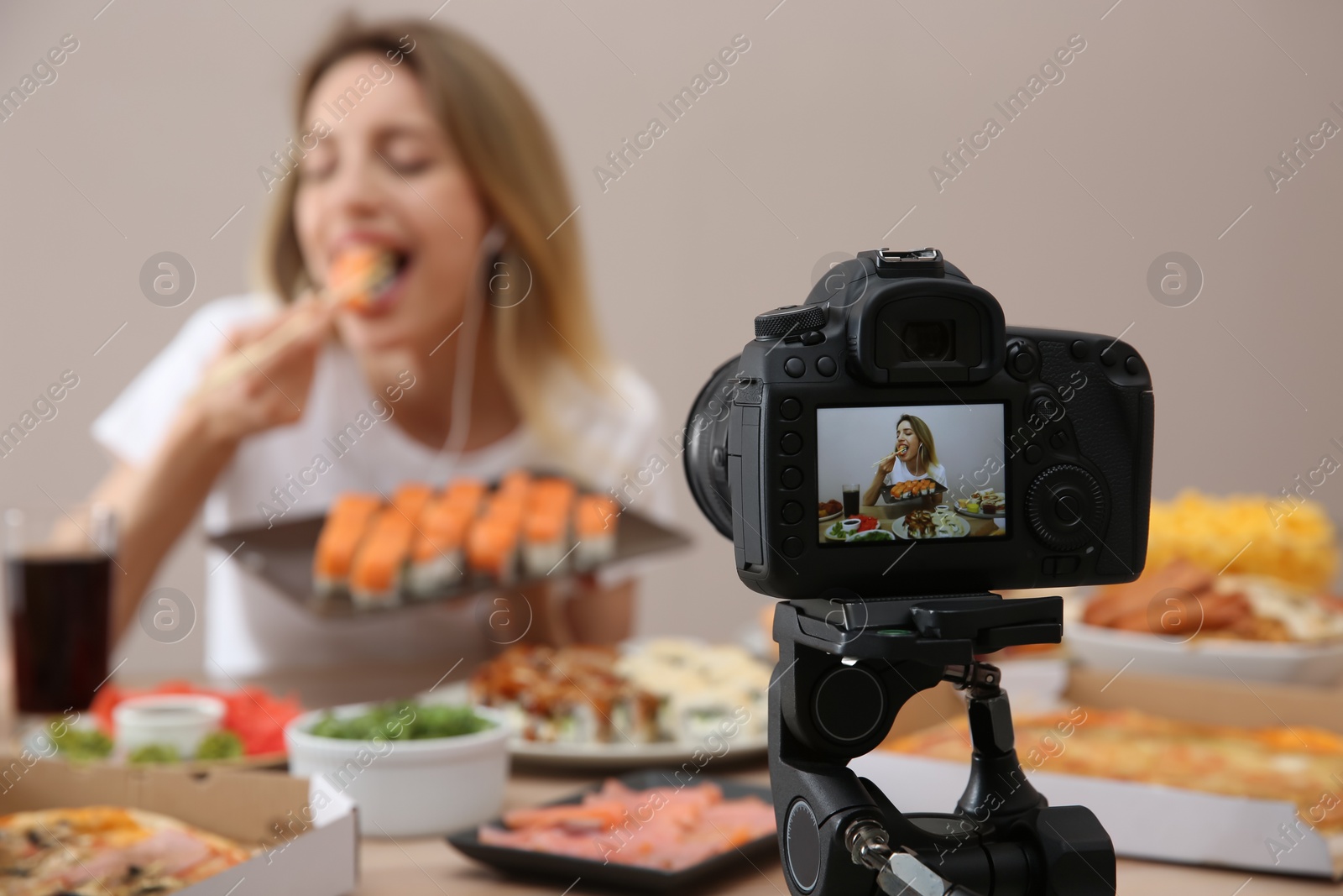 Photo of Food blogger recording eating show against beige background, focus on camera screen. Mukbang vlog