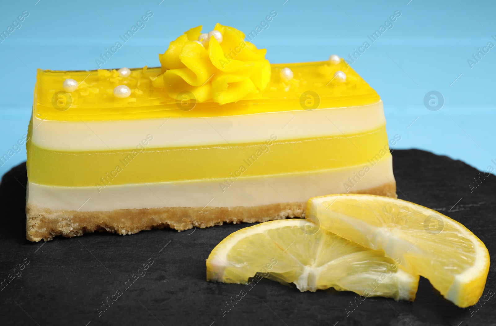 Photo of Delicious cheesecake with lemon on black serving board, closeup