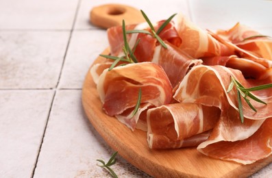 Photo of Slices of tasty cured ham and rosemary on tiled table, closeup. Space for text