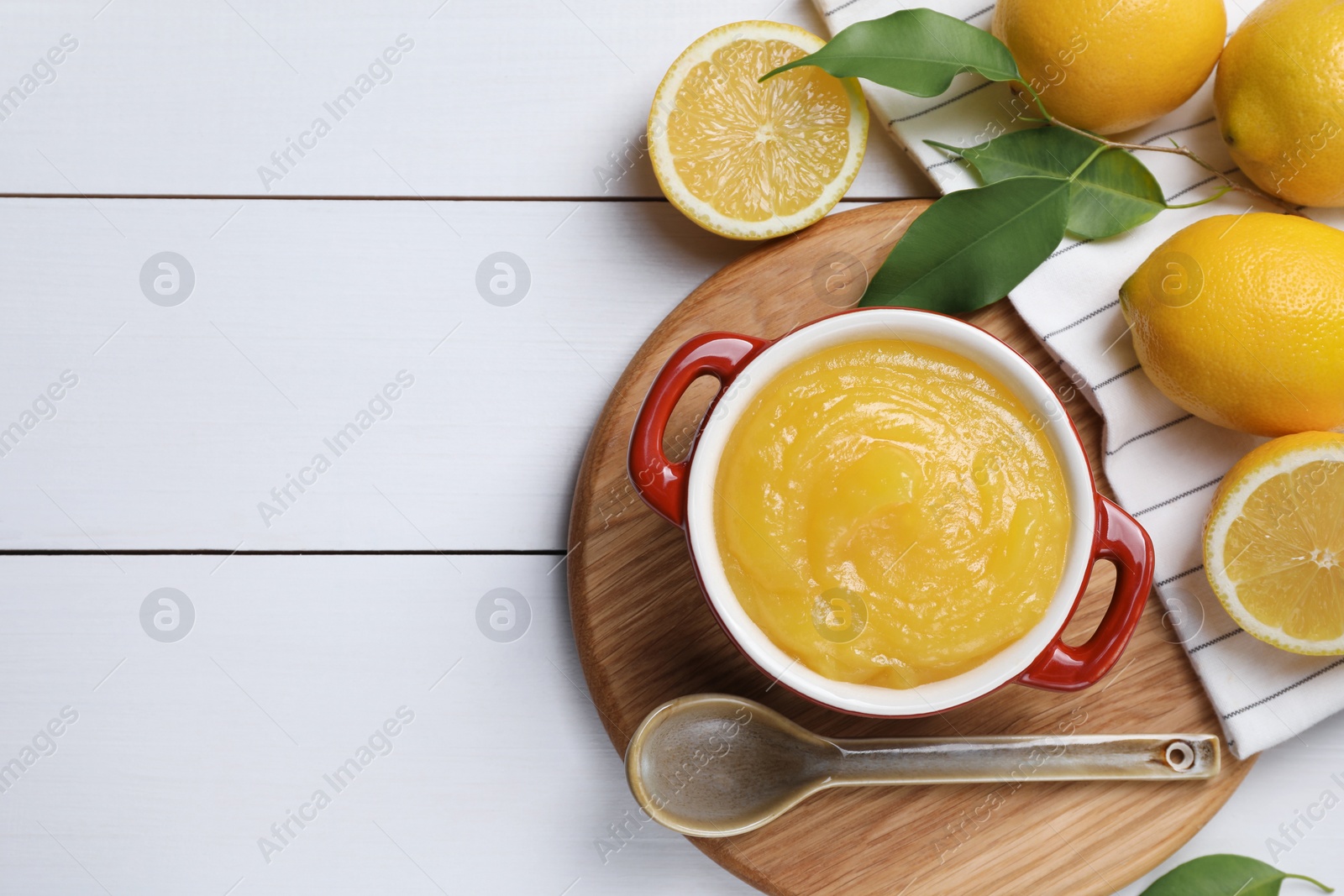 Photo of Delicious lemon curd in bowl, fresh citrus fruits and spoon on white wooden table, flat lay. Space for text