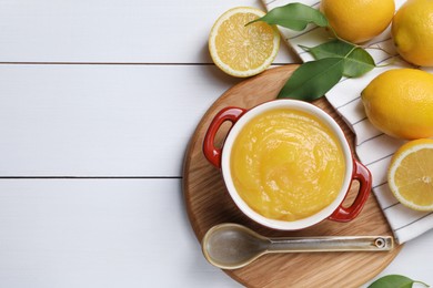 Photo of Delicious lemon curd in bowl, fresh citrus fruits and spoon on white wooden table, flat lay. Space for text