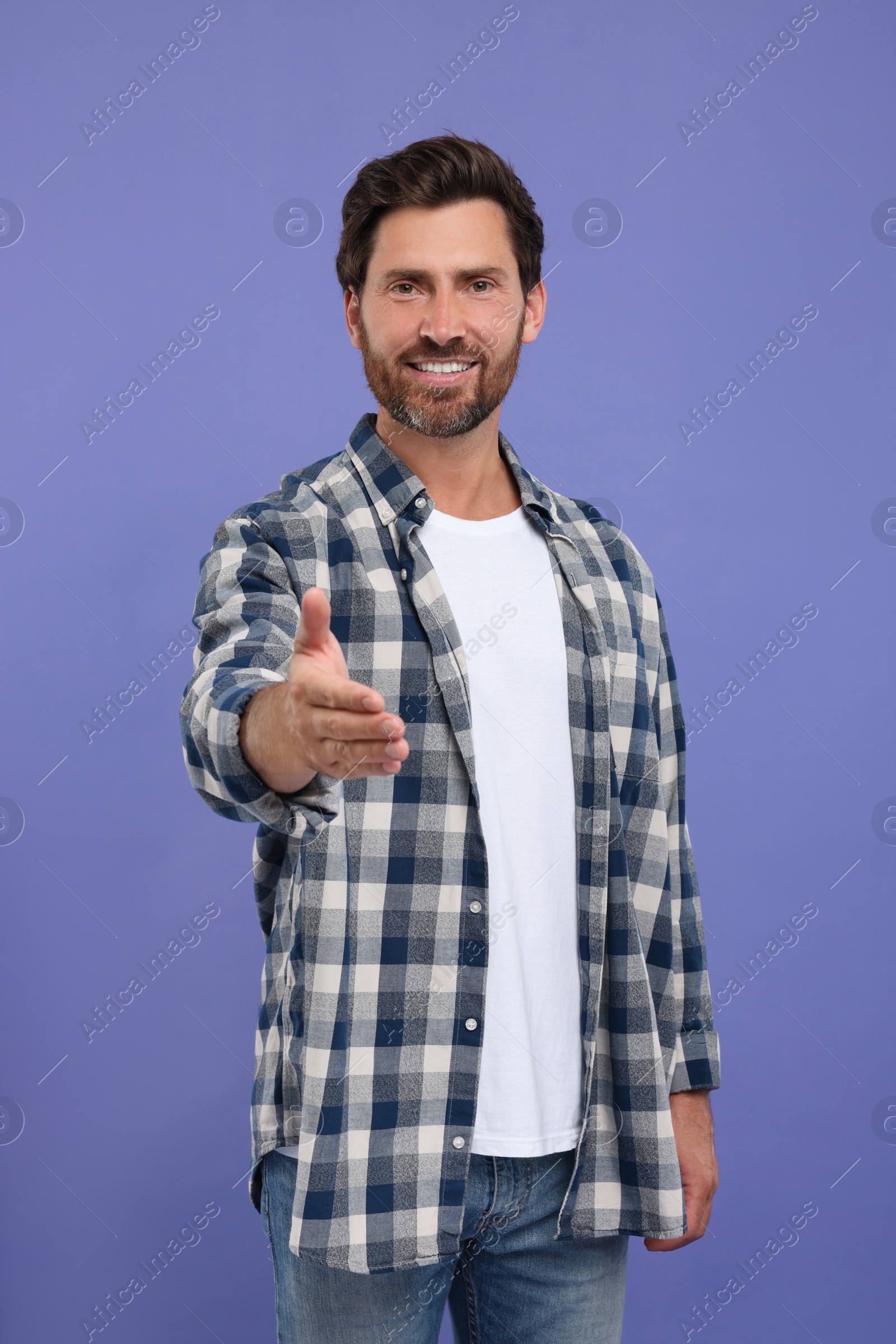 Photo of Happy man welcoming and offering handshake on purple background